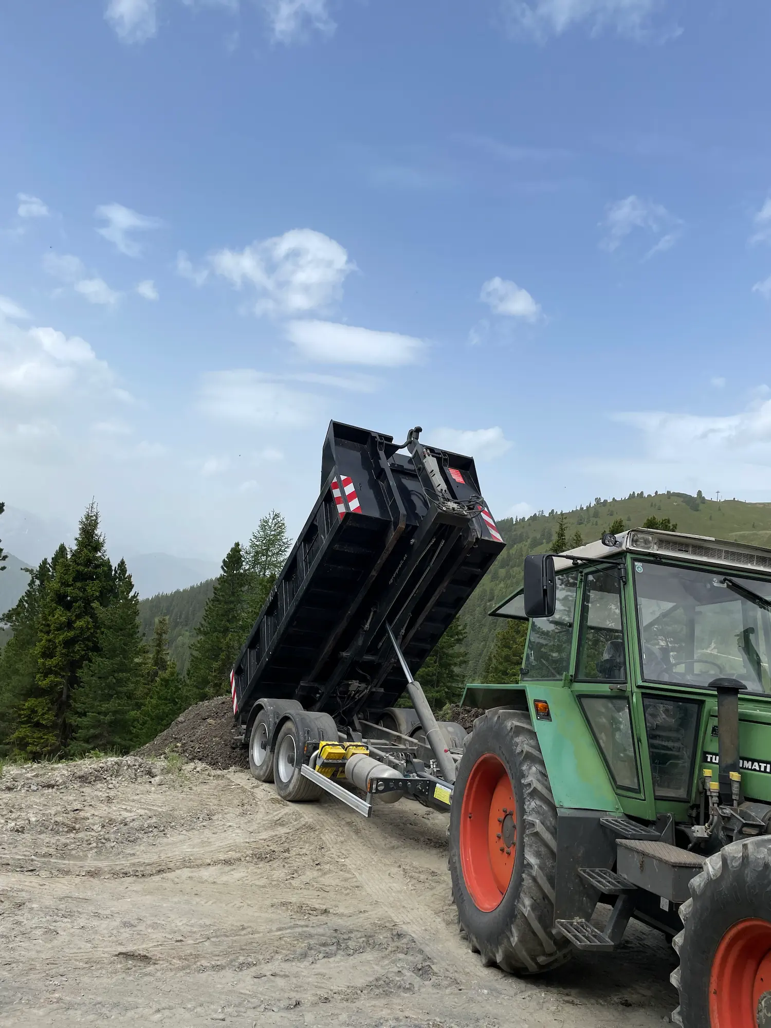 Das Bild zeigt einen Traktor mit Kipper beim Transport von Schotter.